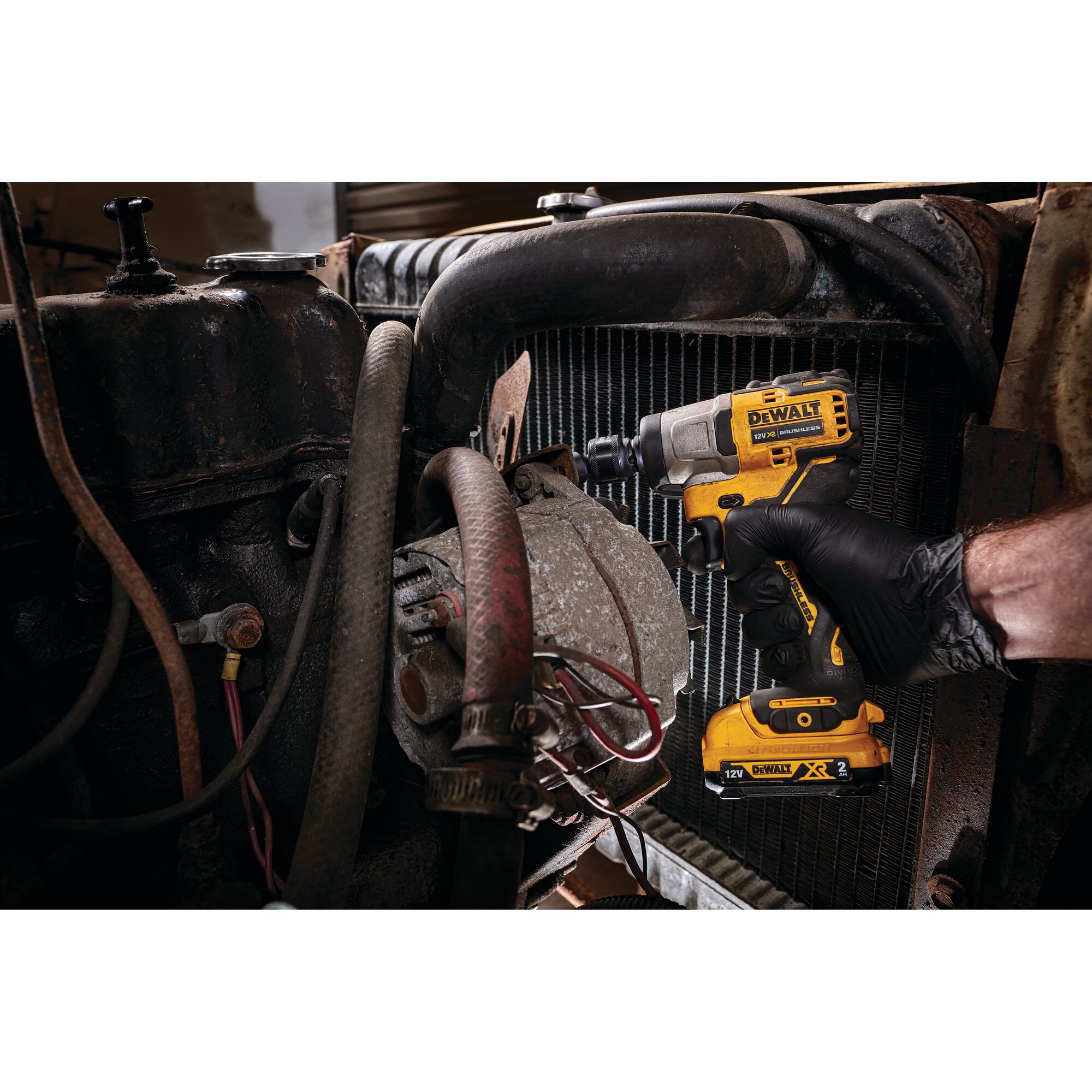 A person using a DEWALT DCF902D2 cordless impact wrench to work on a part of a vehicle engine. The person is wearing a black glove and the tool is yellow and black.