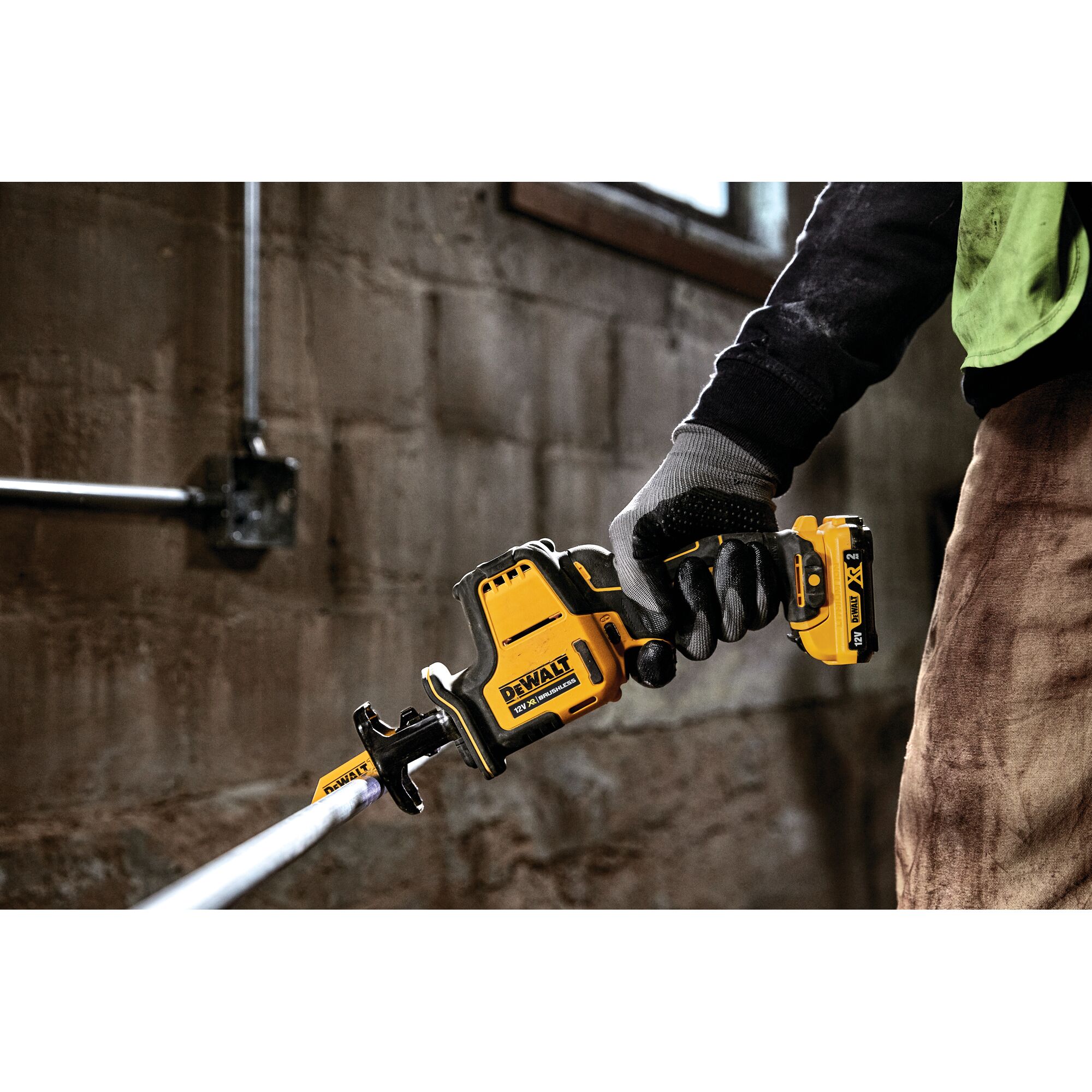 Gloved hand holding a DEWALT DCS312D2 cordless reciprocating saw cutting a metal pipe indoors.