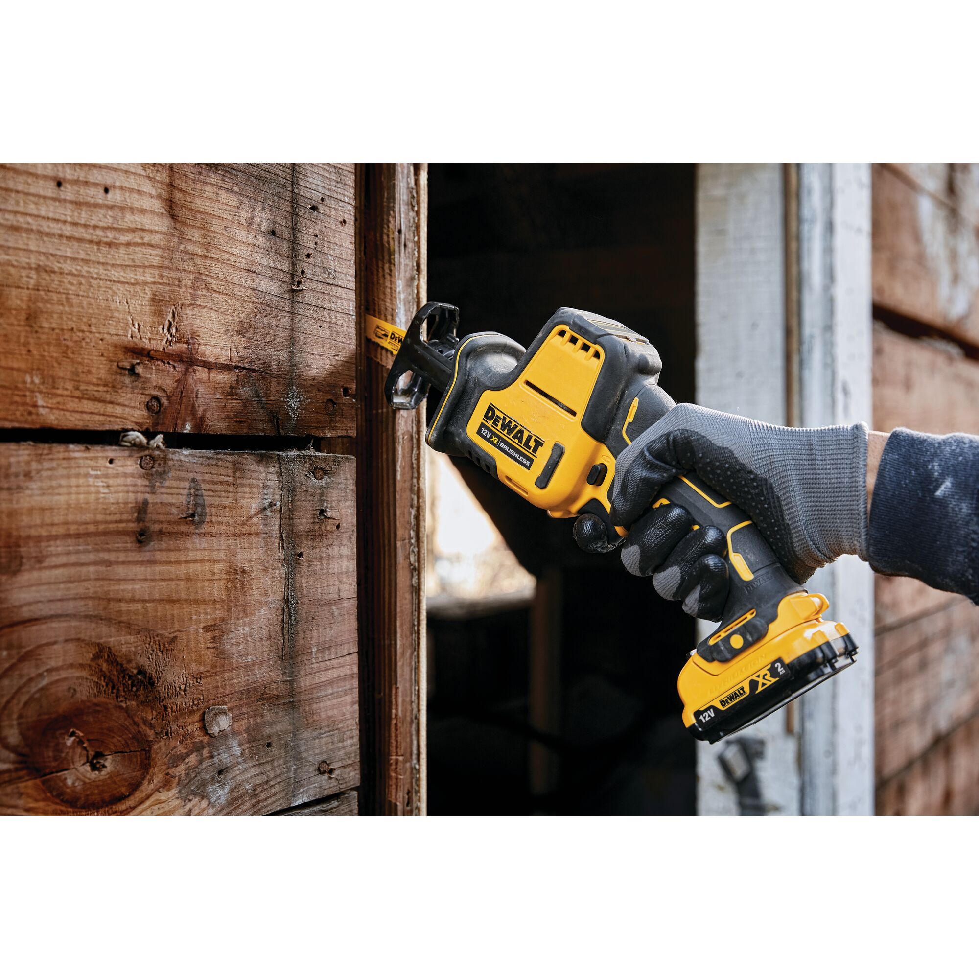 DEWALT cordless reciprocating saw cutting wood, held by a gloved hand near a wooden wall.