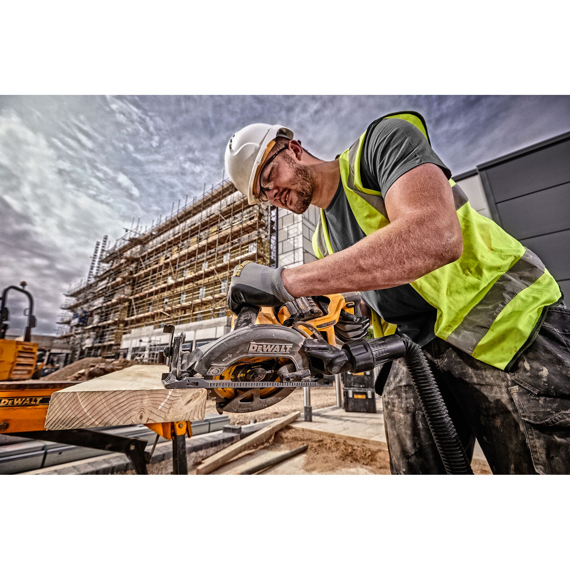 Worker uses DEWALT circular saw DCS577N to cut wood at a construction site, wearing safety gear and gloves.