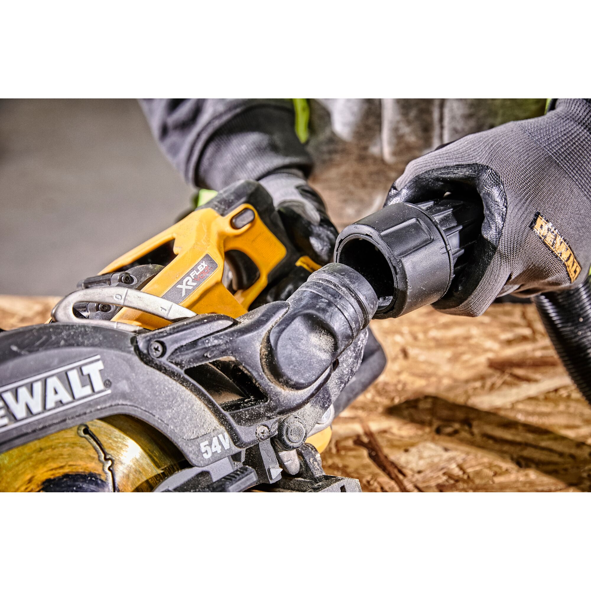 Hands connect a dust extractor to a DEWALT circular saw, shown on a wooden surface during work.