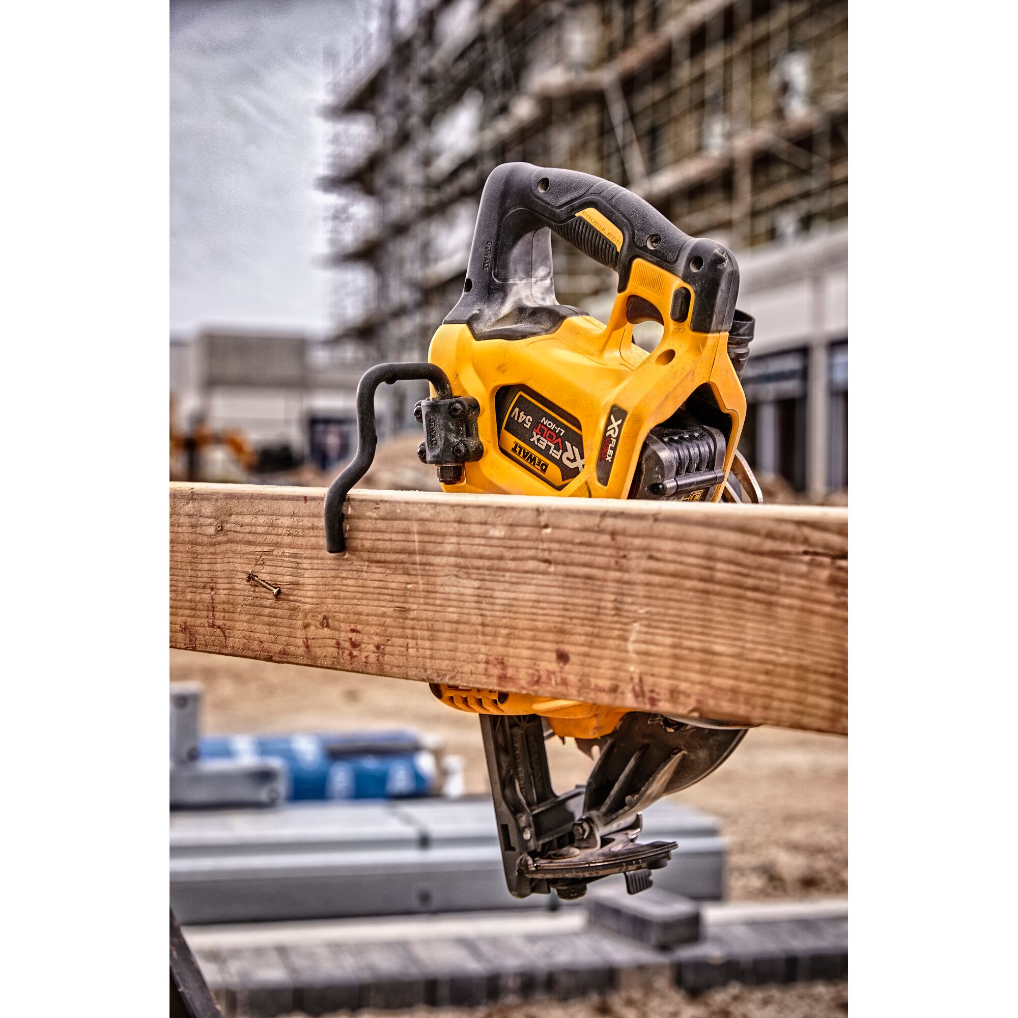 DEWALT DCS577N circular saw resting on wooden beam at a construction site, with scaffolding in the background.
