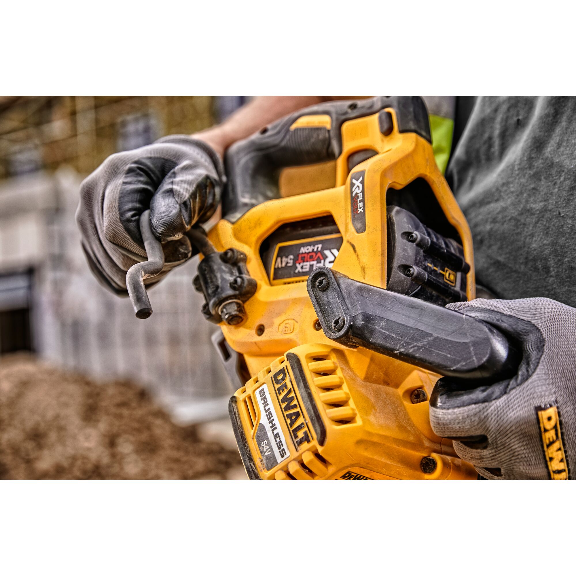 Close-up of DEWALT DCS577N power tool held by gloved hands, showing details and branding at a worksite.