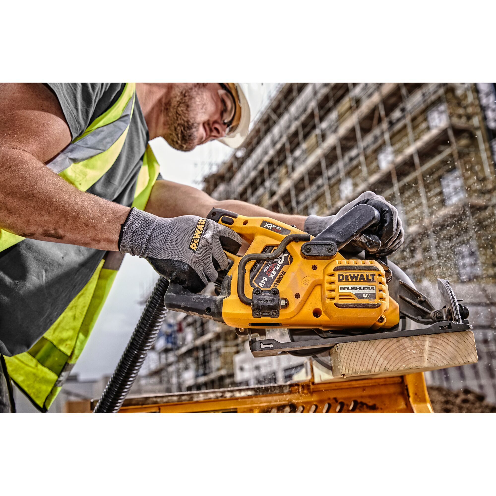 Worker using a DEWALT cordless saw to cut wood on a construction site, wearing gloves and a safety vest.