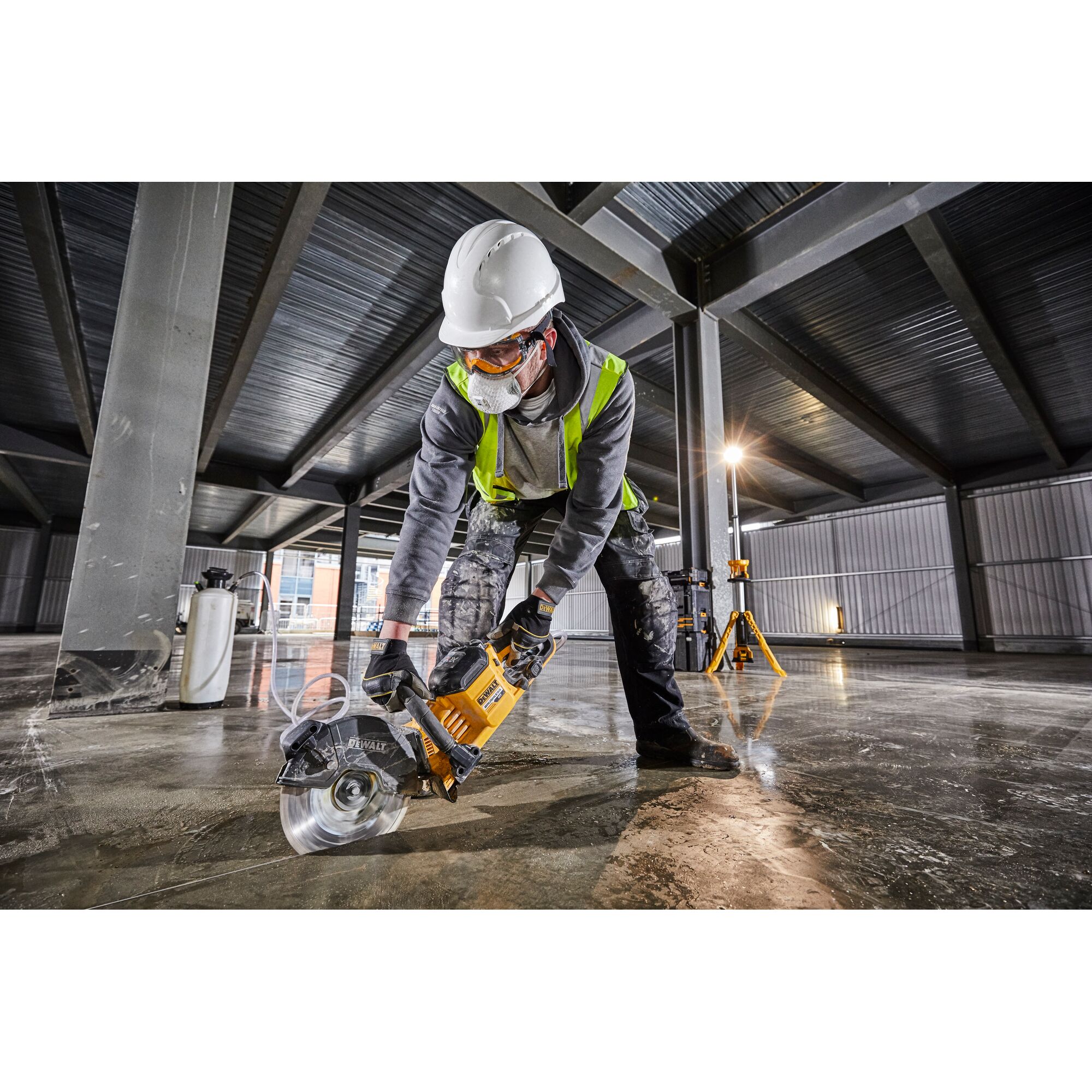 Worker with safety gear uses a DEWALT DCS690N power saw to cut concrete on a construction site indoors.