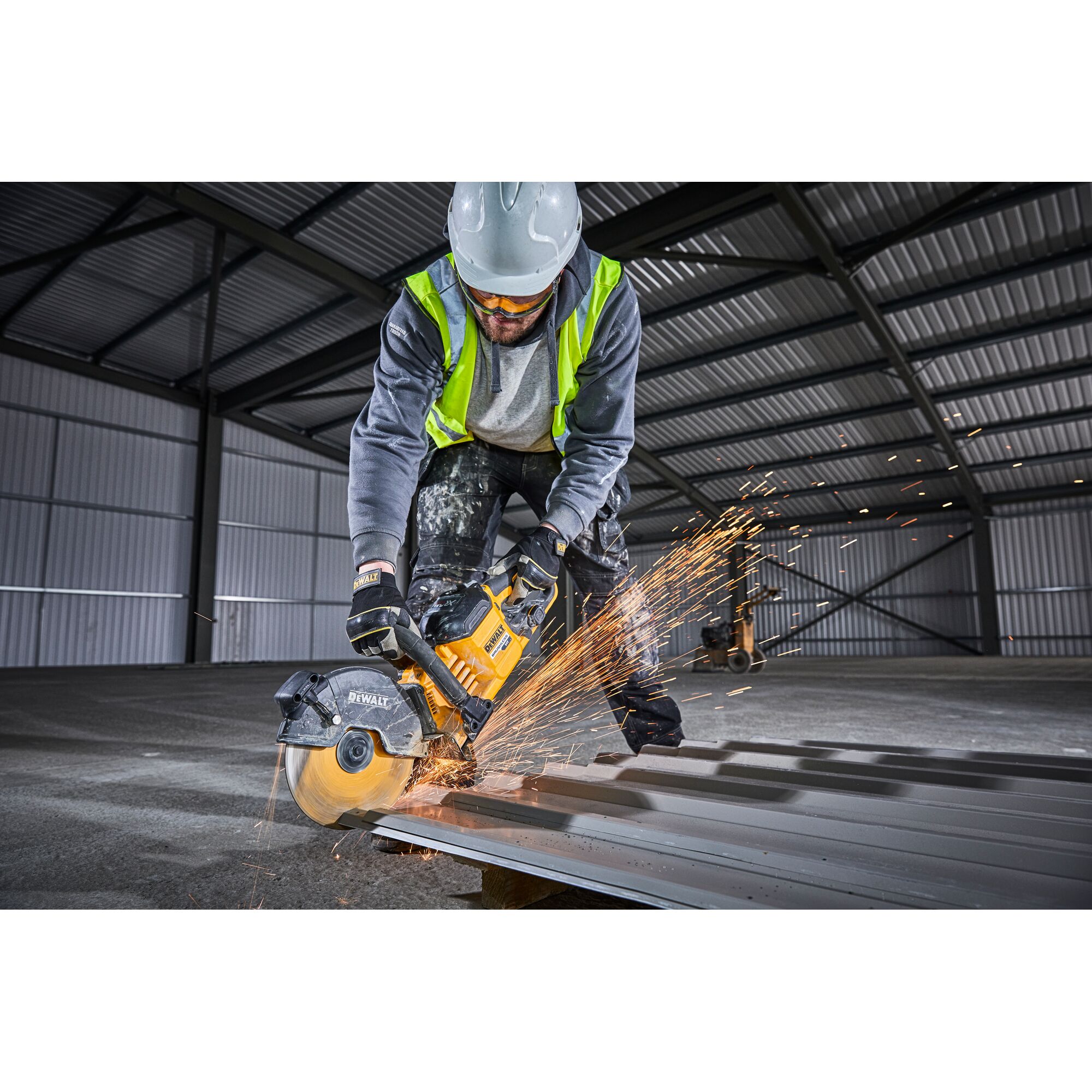 Worker using DEWALT DCS690N saw to cut metal roofing, sparks flying, in an industrial warehouse.