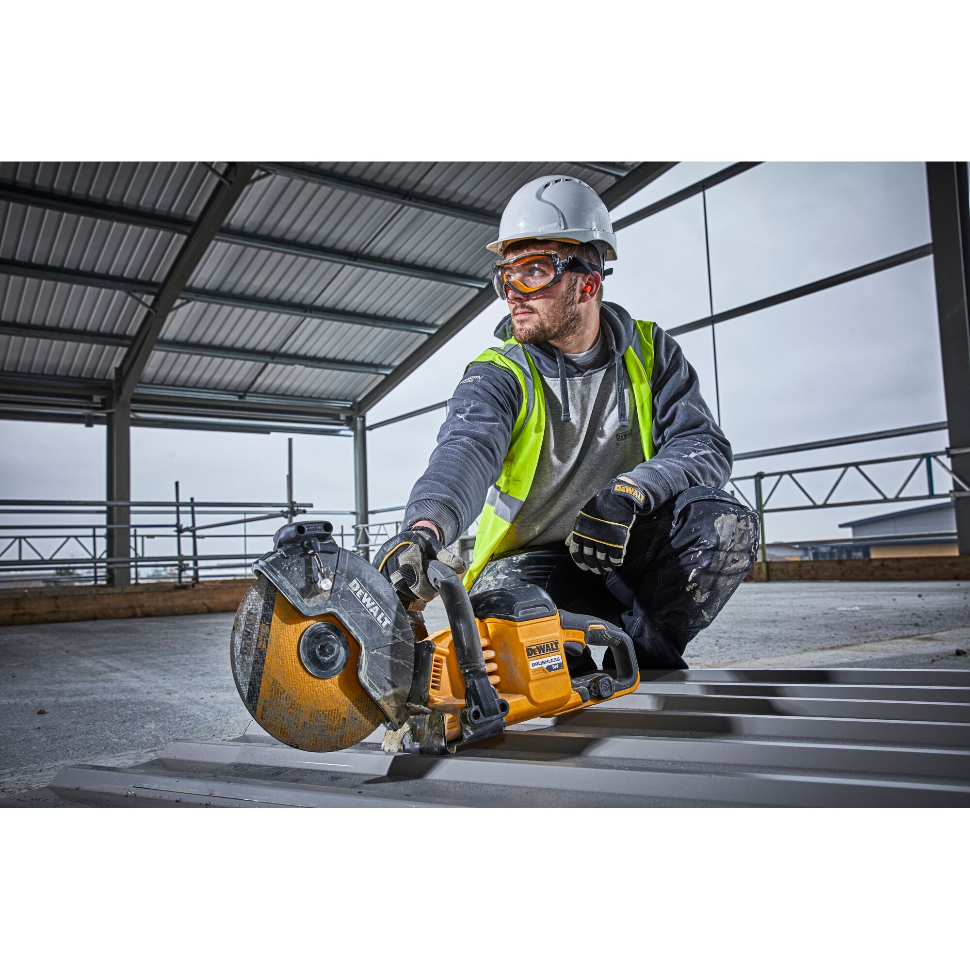 Worker uses DEWALT DCS690N saw to cut metal sheet on construction site, wearing helmet and safety vest.