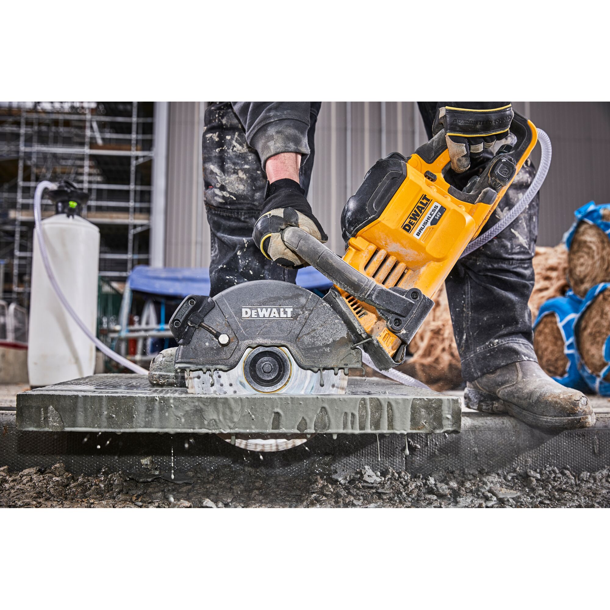 Person uses DEWALT DCS690N power saw to cut stone outdoors; water cools the blade during operation.