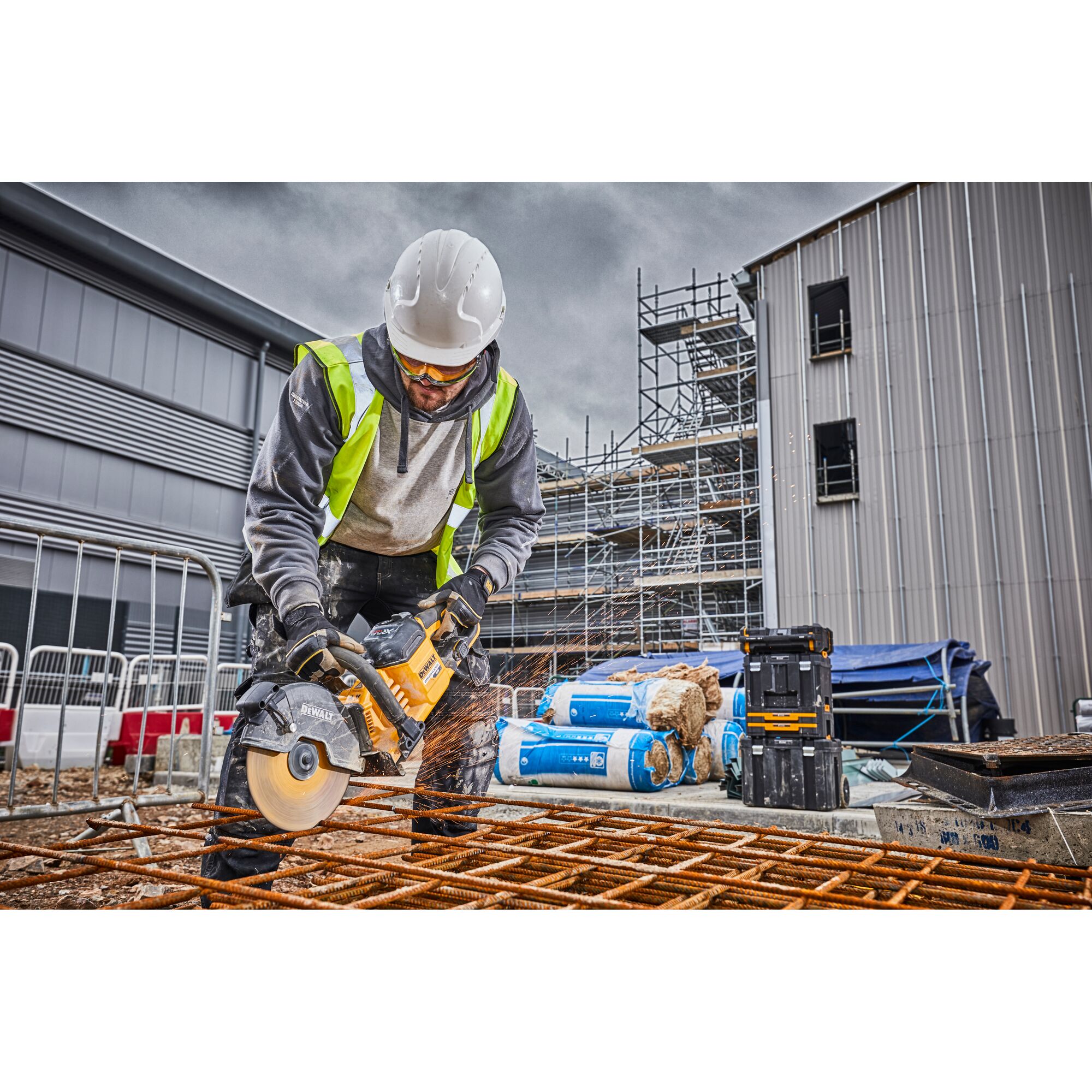 Worker using a DEWALT DCS690N saw to cut metal rods on a construction site with safety gear and equipment.