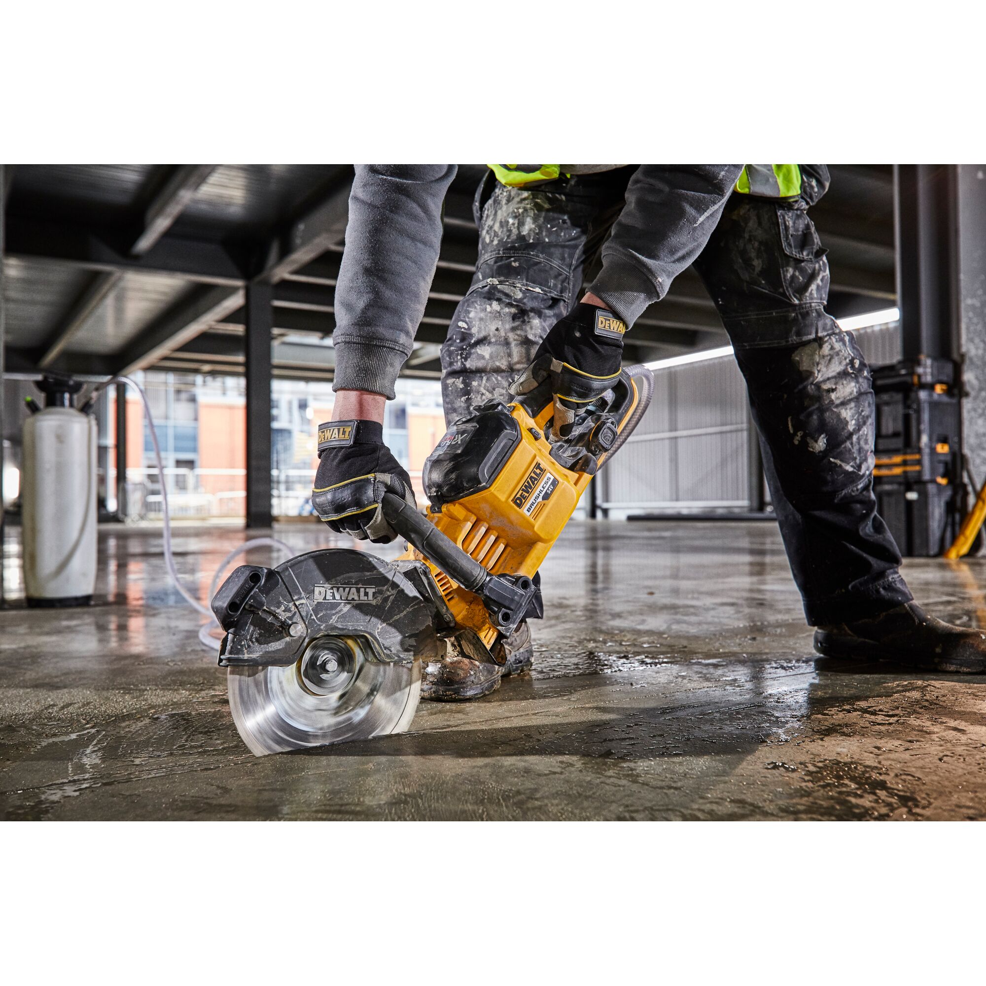 Worker using a DEWALT DCS690N saw to cut concrete floor at construction site, wearing gloves and protective clothing.