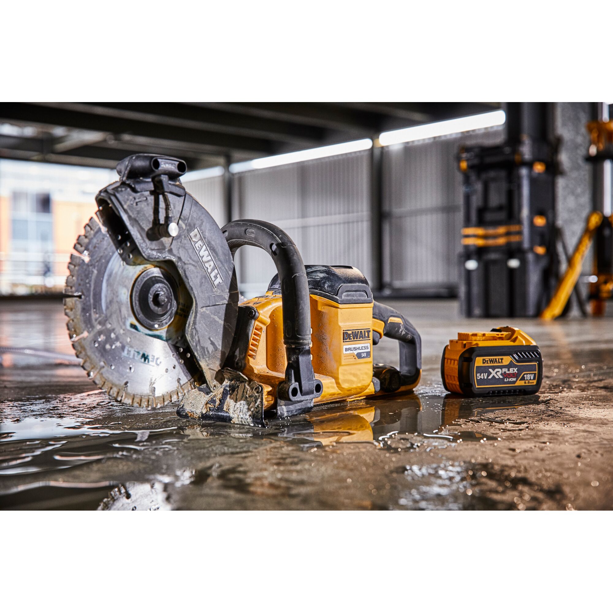 Dewalt cordless cut-off saw and battery on wet concrete floor in industrial workshop setting.