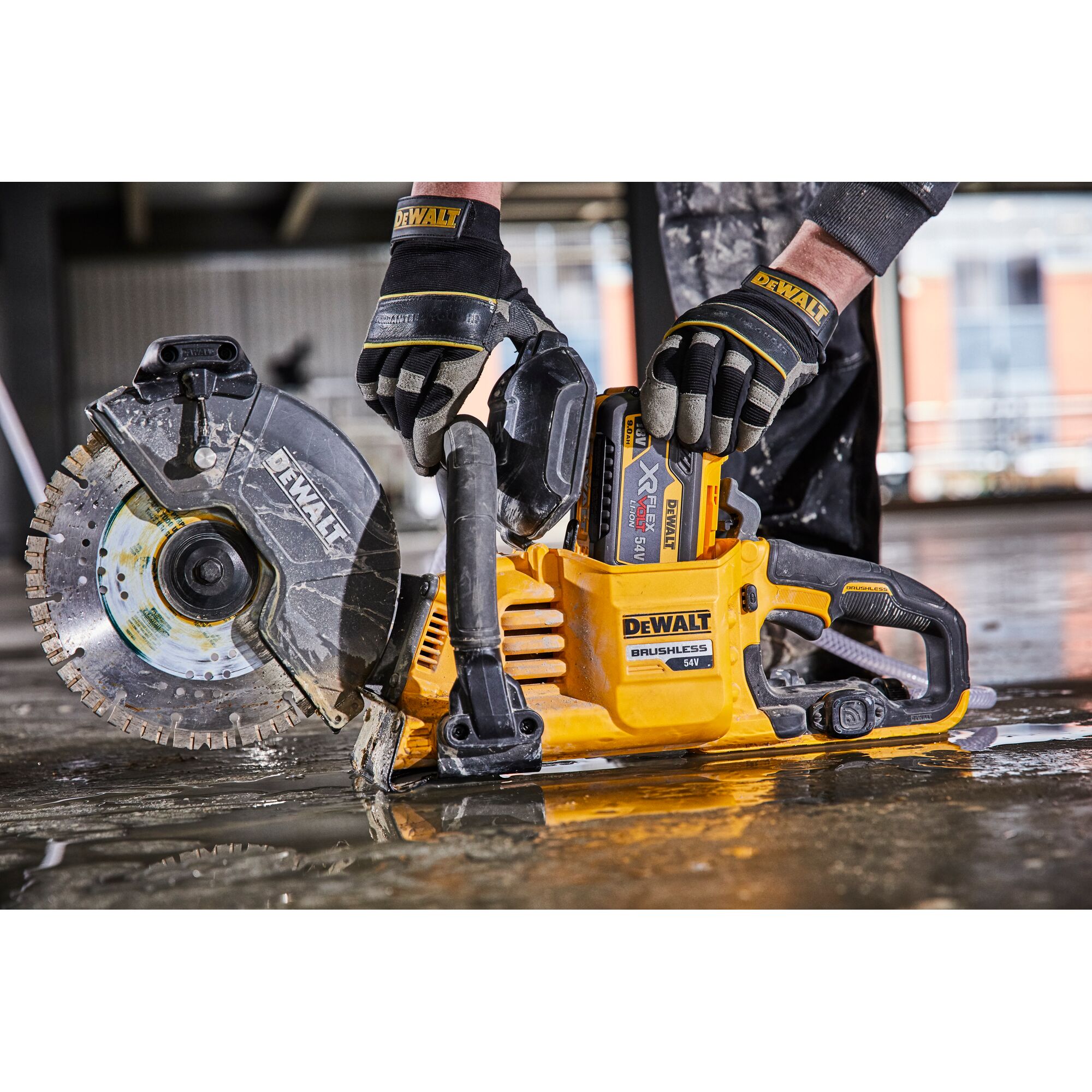 DEWALT brushless 54V cutting tool in use by gloved hands on a wet concrete surface.