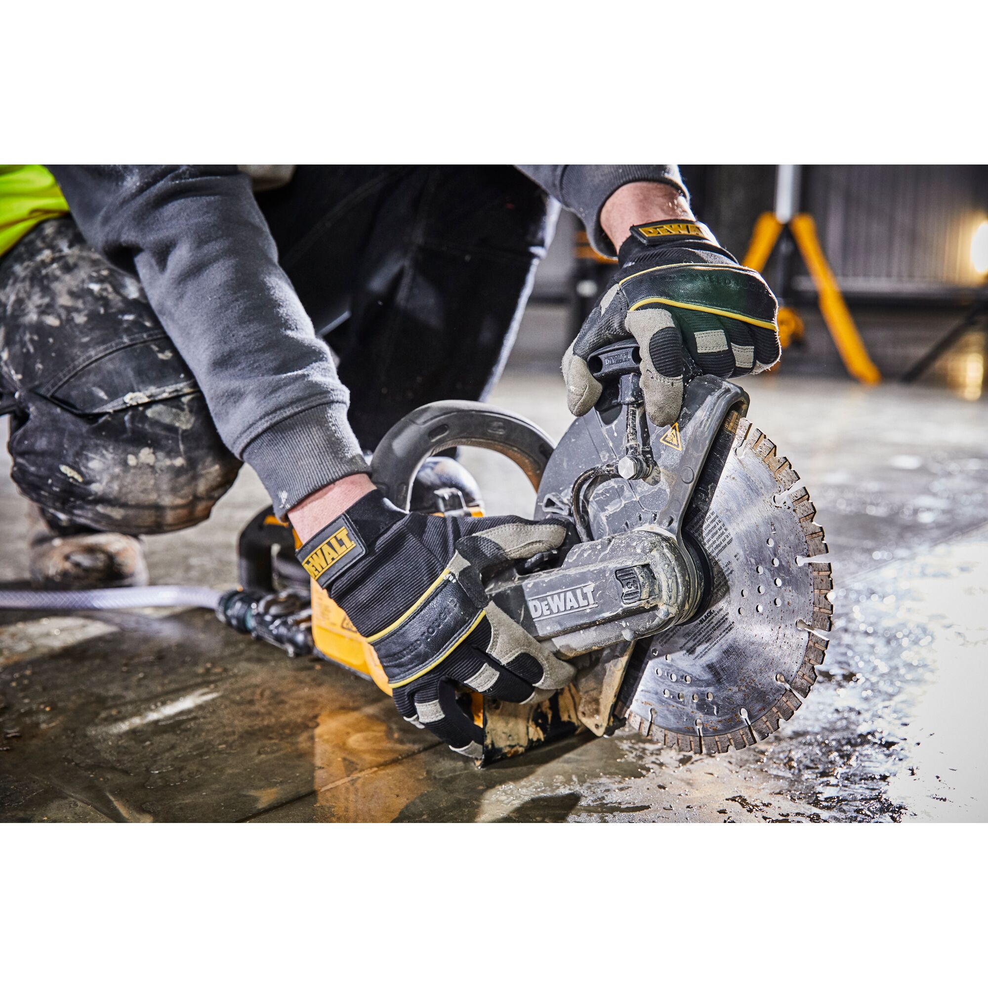 DEWALT worker uses power cut-off saw on wet concrete floor, wearing gloves and work clothes.