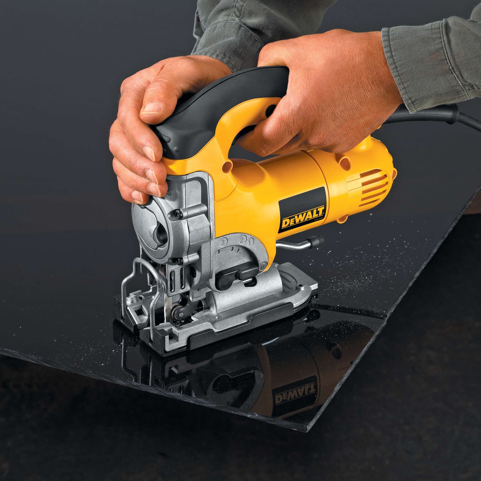 Close-up view of hands using a yellow and black DEWALT electric jigsaw to cut through a dark sheet of material.