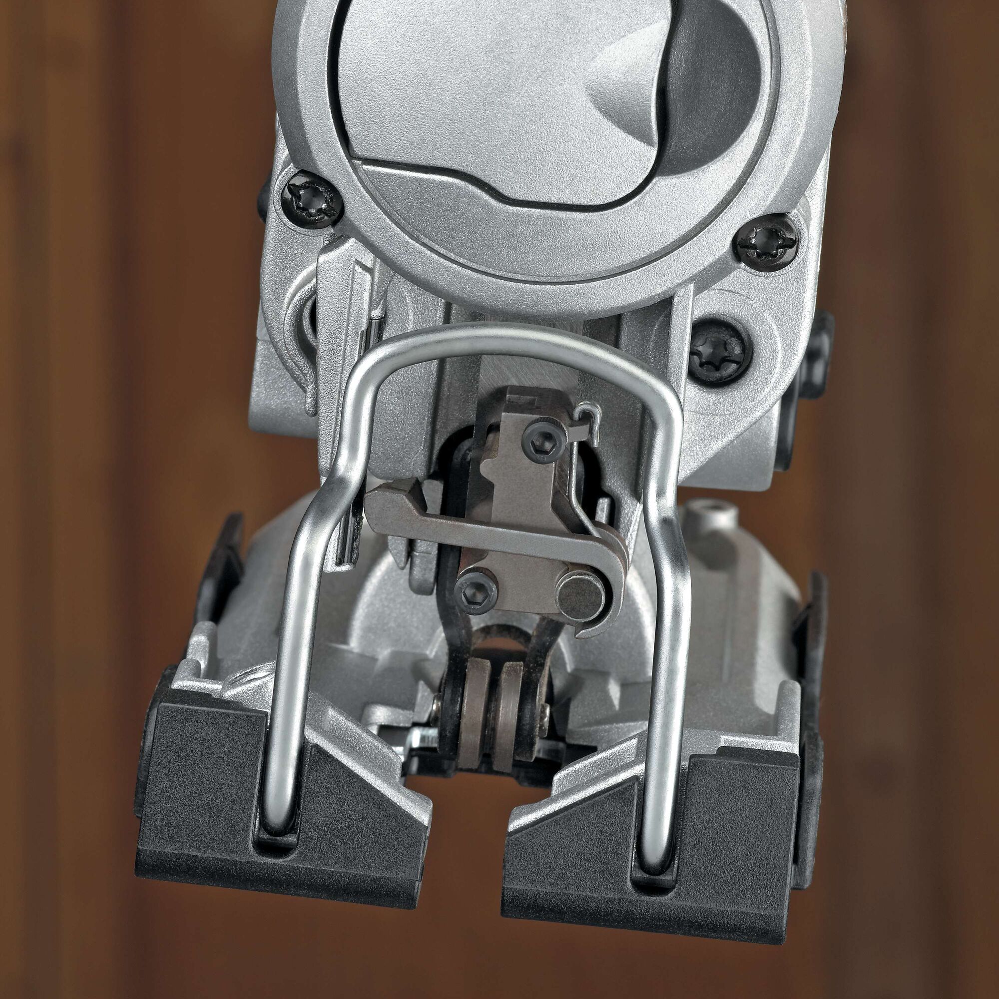 Close-up view of the lower part of a DEWALT jigsaw power tool, showing its metal blade guard, adjustment mechanism, and base plate against a blurred brown background.
