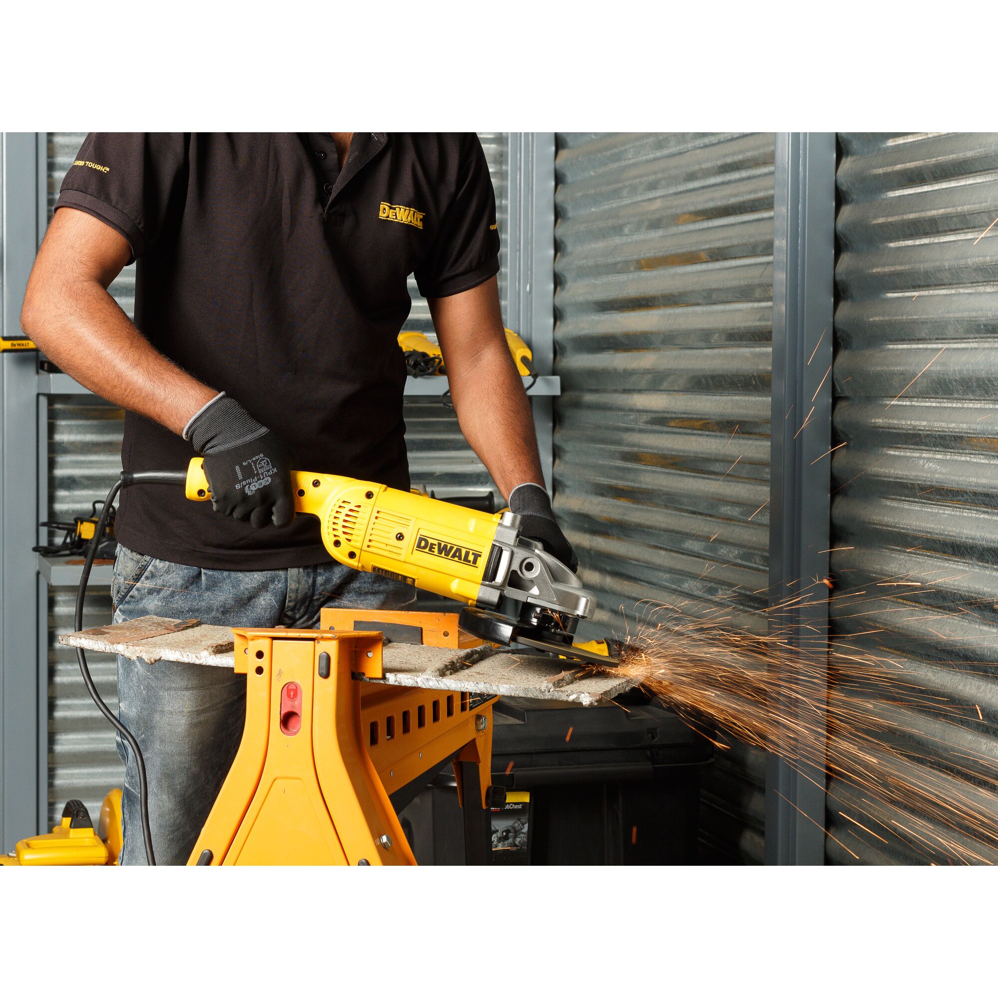 A person wearing gloves and a black shirt uses a yellow DEWALT DWE493 angle grinder to cut a metal piece, causing sparks to fly, in a workshop setting.