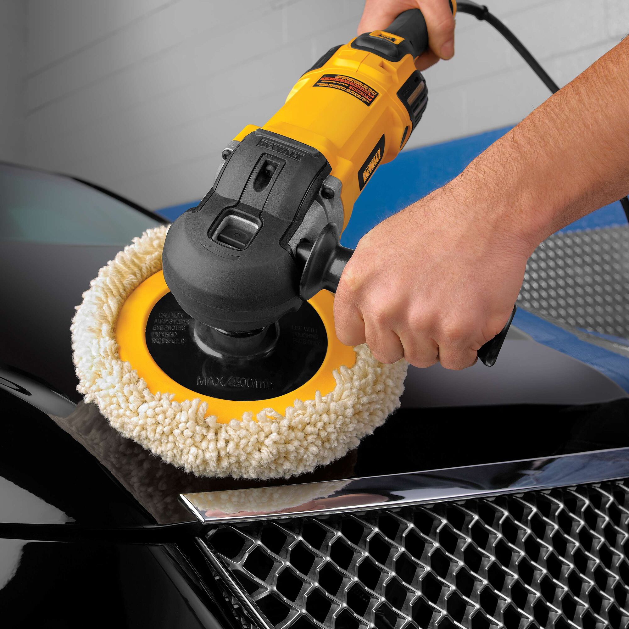 A close-up view of a person using a DEWALT DWP849X power polisher with a wool pad to polish the hood of a black car.