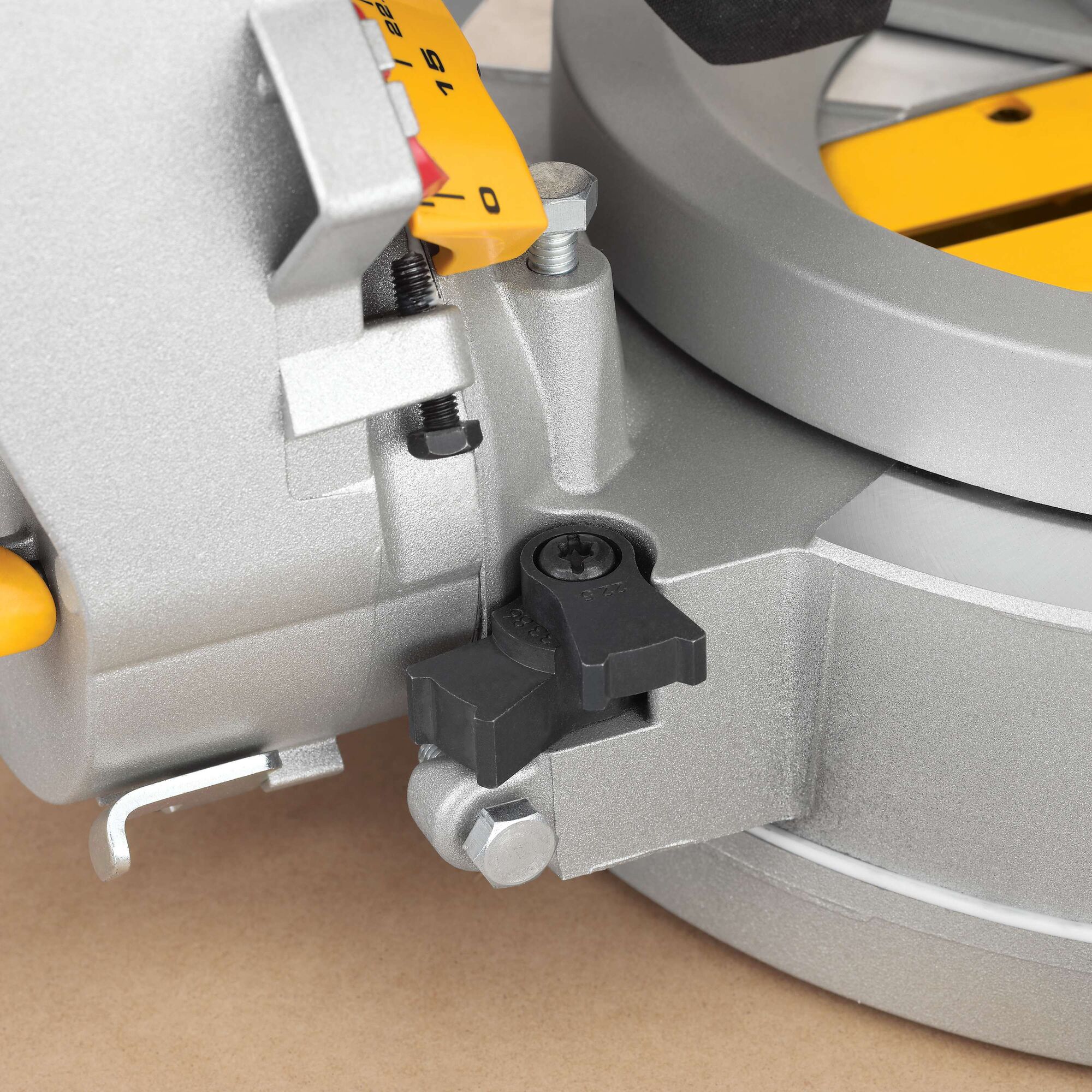 Close-up view of the adjustment mechanism and locking knob of a DEWALT DWS780 miter saw, showing the metal parts and the yellow angle scale.