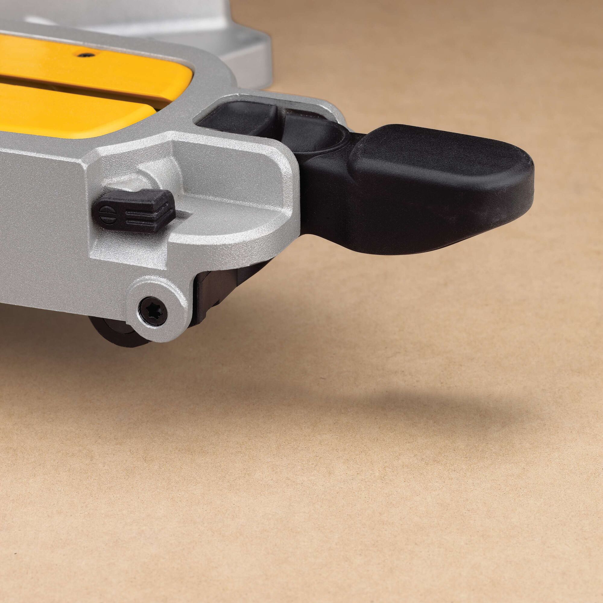 Close-up of a DEWALT miter saw part, featuring a silver metallic frame, a yellow component, and a black handle on a beige surface.