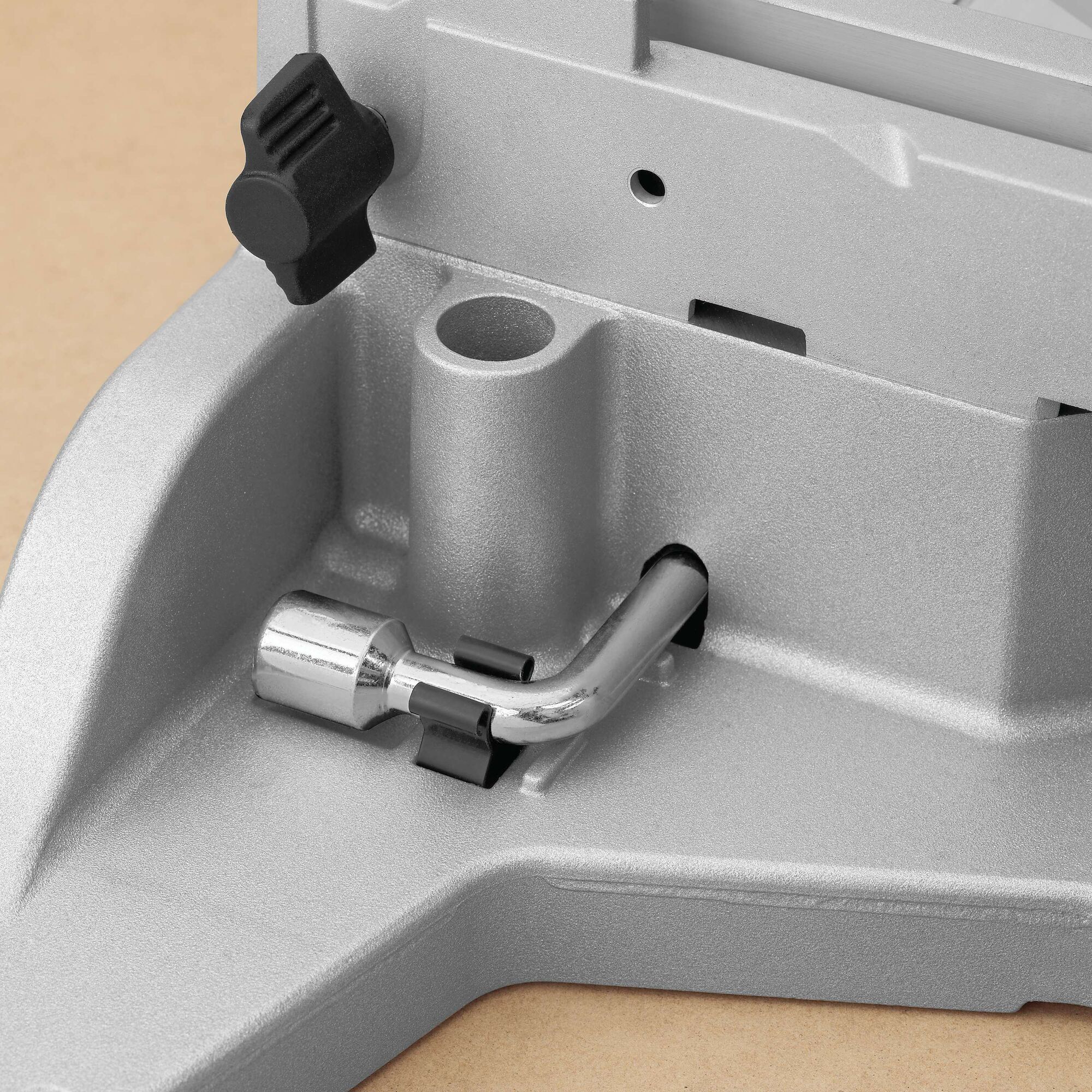 Close-up view of a metallic component on a DEWALT miter saw, focusing on the base with an adjustment knob and a silver cylindrical part attached to a curved metal rod.